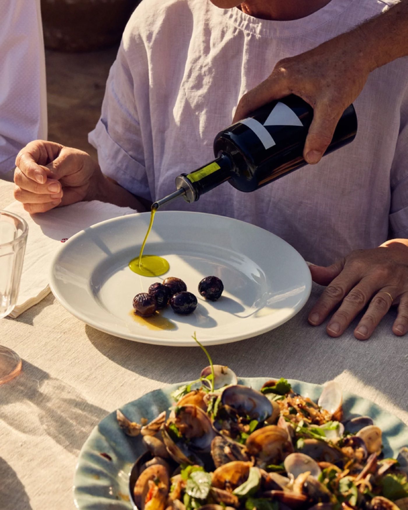 Jdoudna olive oil being poured over olives on a plate at an outdoor table