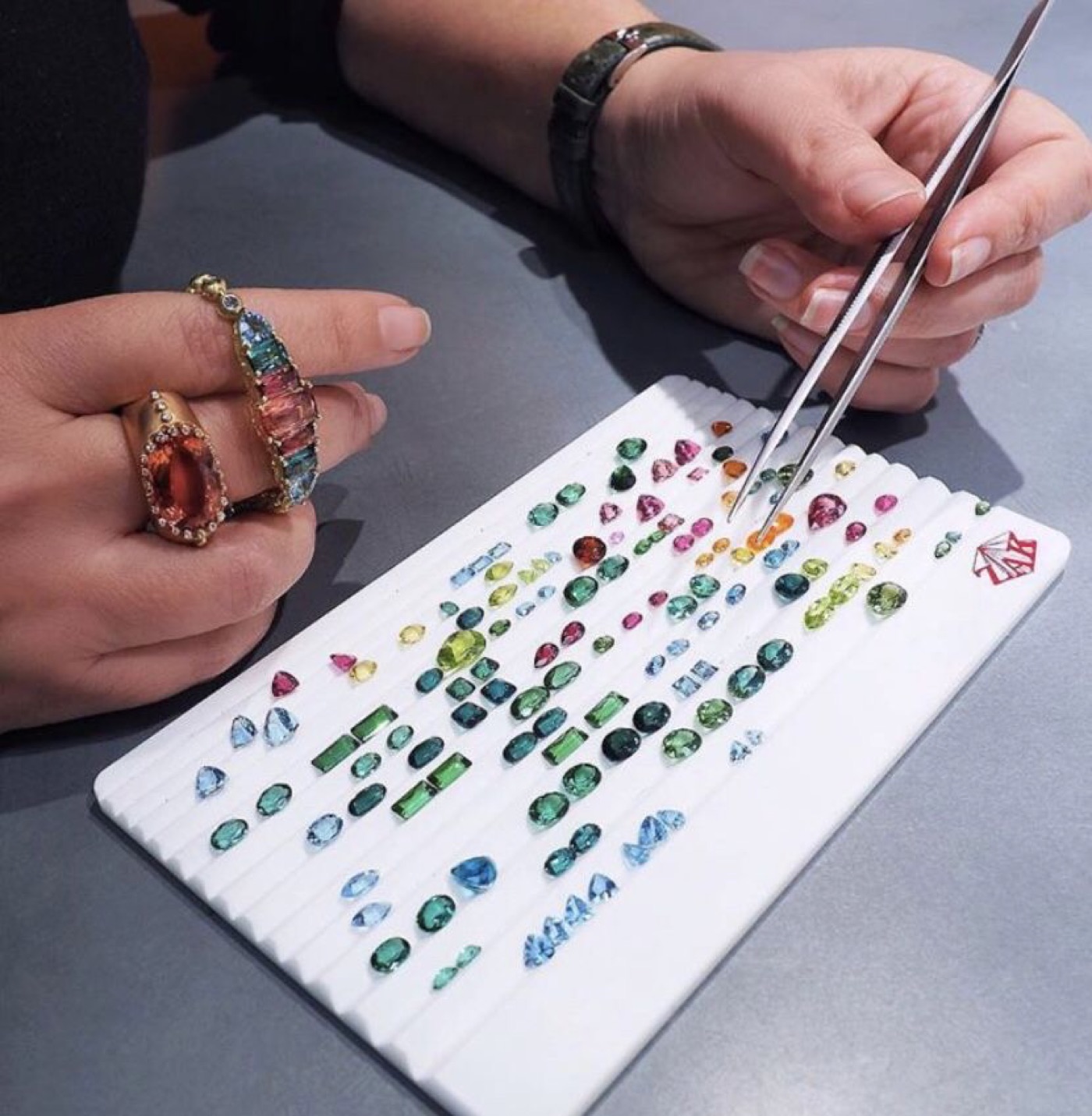 Loose coloured gemstones being sorted by hand with tweezers on a ribbed jeweler's tray