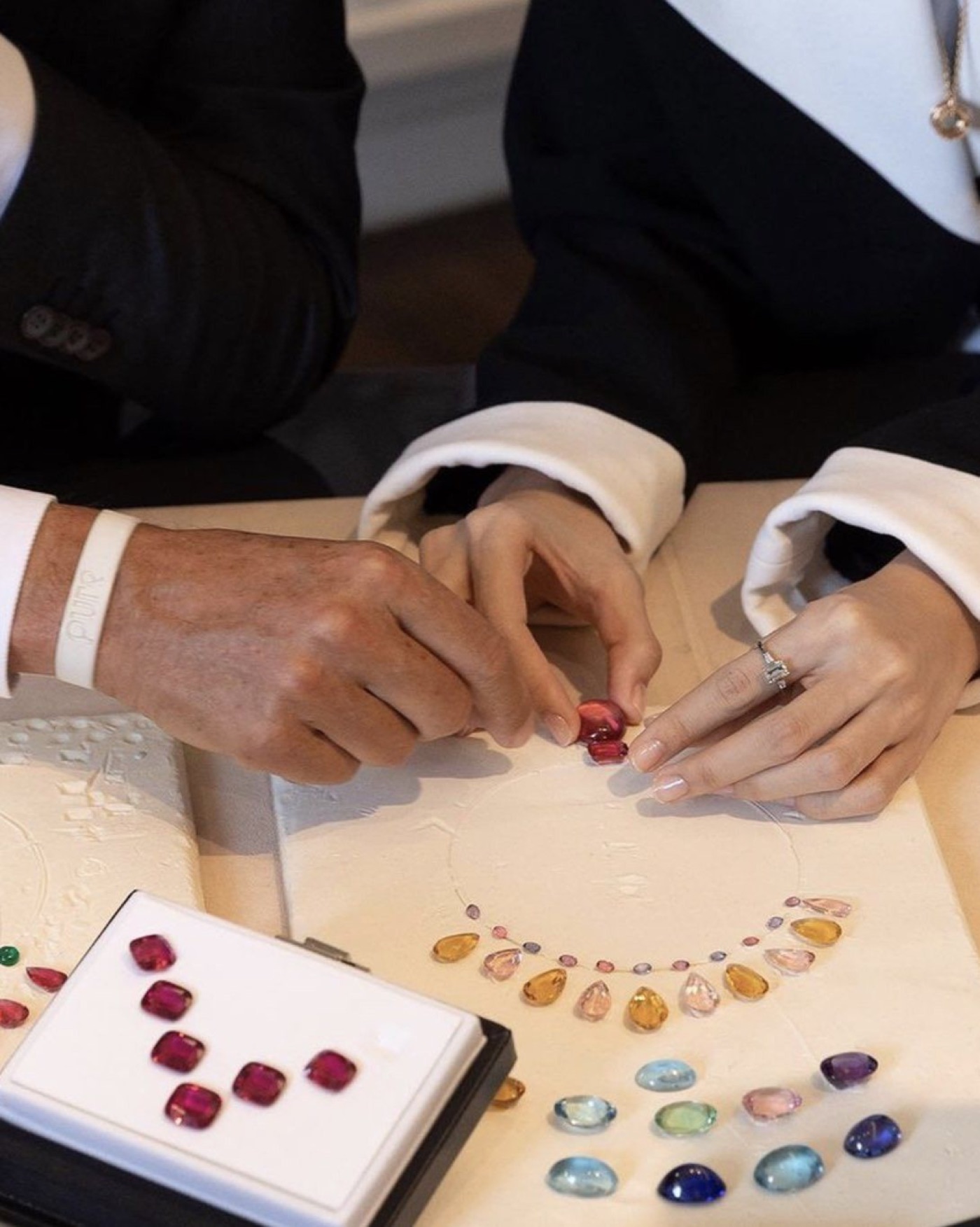 Jeweler's hands arranging a coloured gemstone necklace design on a workbench